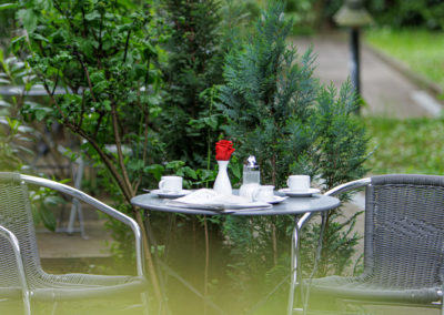 Gedeckter Tisch mit zwei Stühlen und roter Rose im begrünten Außenbereich | Apart Business Hotel