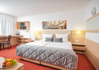 Schlafbereich einer Suite mit Doppelbett, Schreibtisch, Bücherregal und Obstteller | Apart Business Hotel