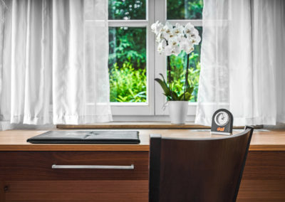 Schreibtisch eines Doppelzimmers mit Stuhl, Orchidee und Wecker vor dem Fenster | Apart Business Hotel